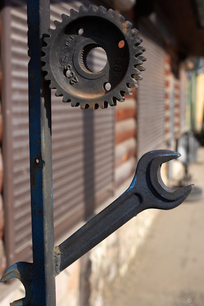 A detailed close-up of a gear and wrench mounted on a metal post outdoors in daylight.